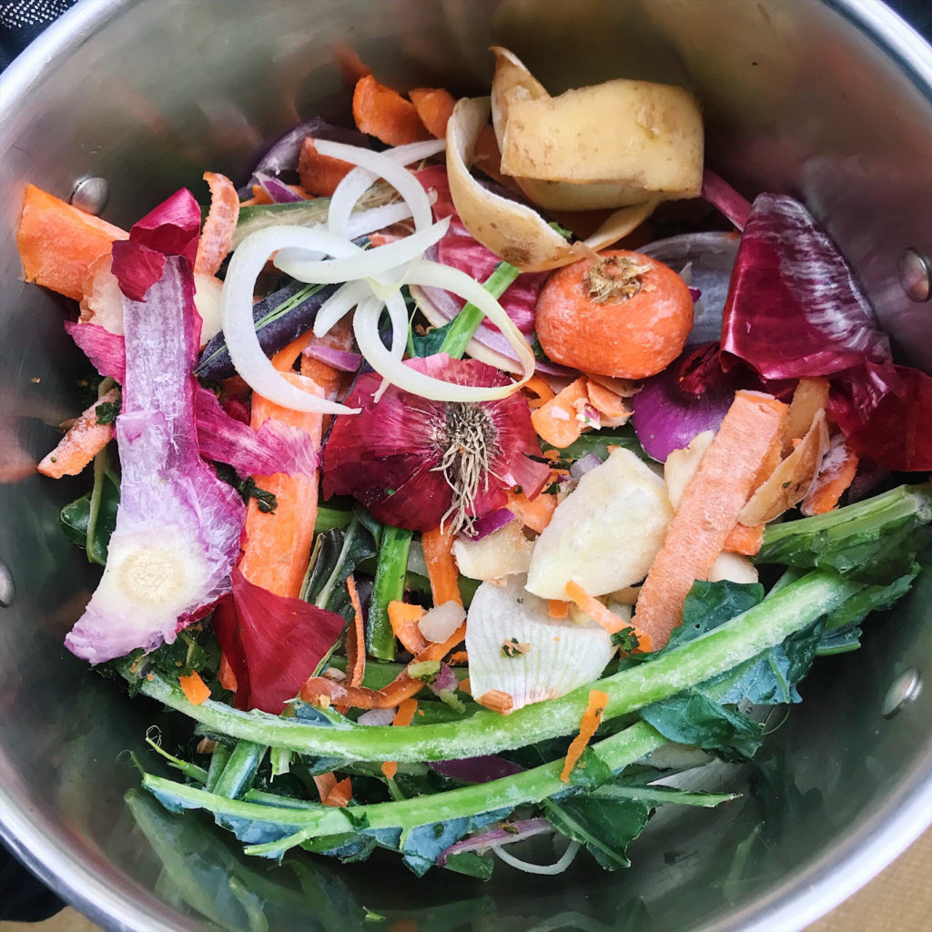 soup pot with veggie scraps inside: carrot tops, onions, and green stems