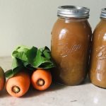 two jars of vegetable broth with greens, carrots and onion next to them on counter