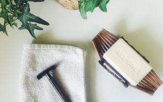 washcloth with a metal razor on top, bar of soap, green plant on white background