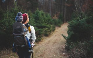 blond woman with baby in carrier on her back walking down path