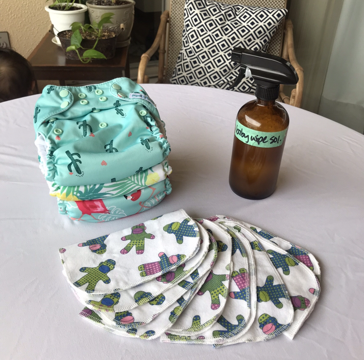 stack of colorful cloth diapers on white table with cloth wipes and brown spray bottle placed next to them